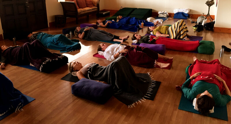 Breathwork session — participants lying on mats with bolsters in a wood-floored room